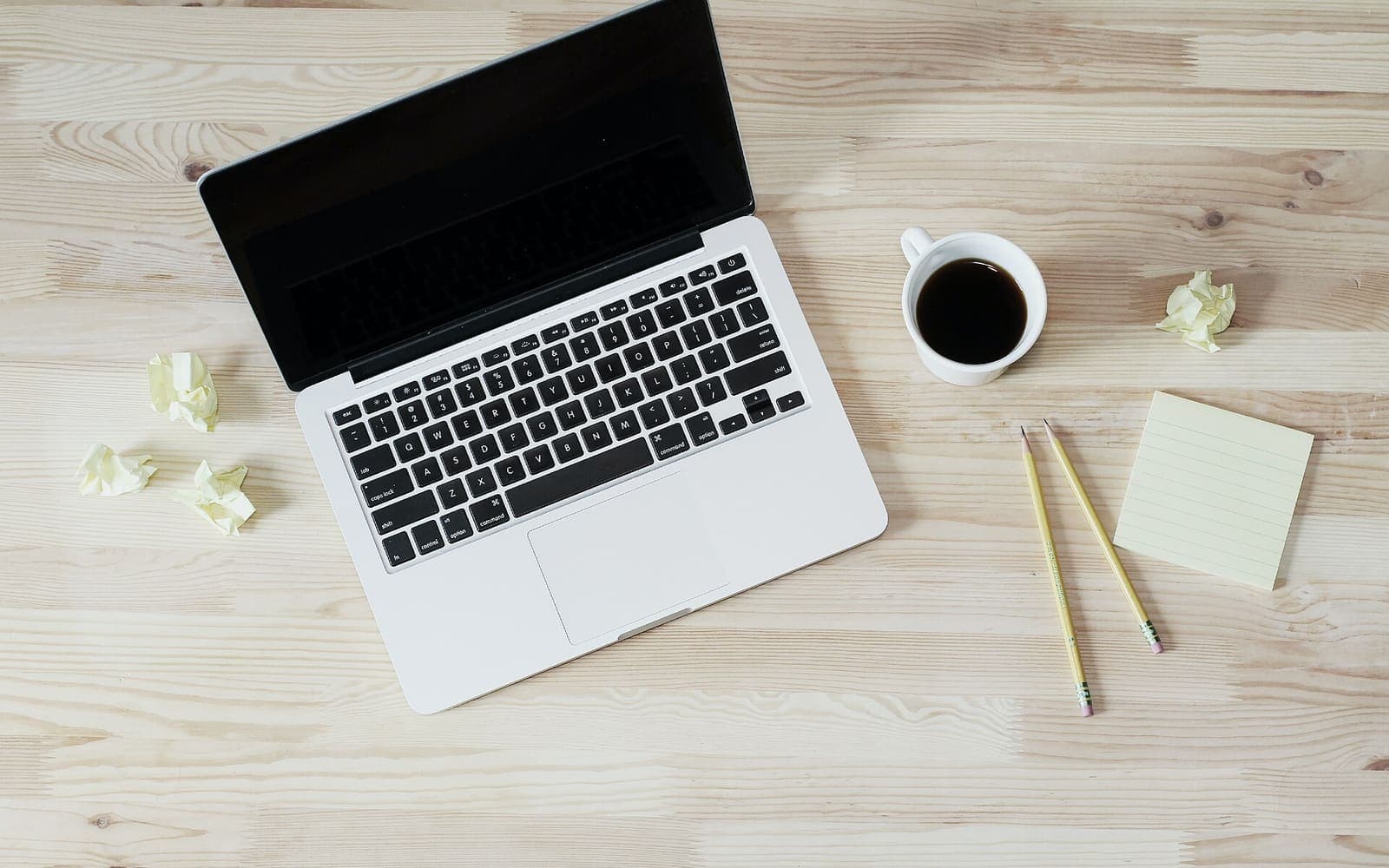 A laptop, coffee and a notepad on a wooden desk